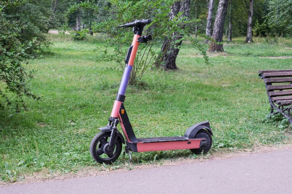 Abandoned electric scooter near the path in a city park. Discharged electric scooter battery. City electric scooter rental service - kicksharing.