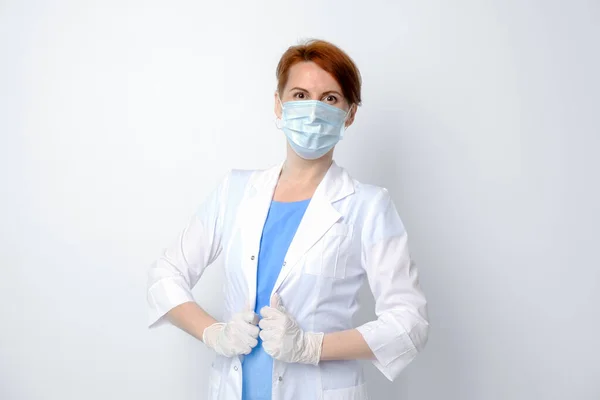 Beyaz tıbbi önlüklü ve koruyucu maskeli genç bir kadın. Beyaz arka planda kadın doktor portresi. Tatmin olmuş tıp öğrencisi. Aile doktoru, terapist, çalışmaya hazır..