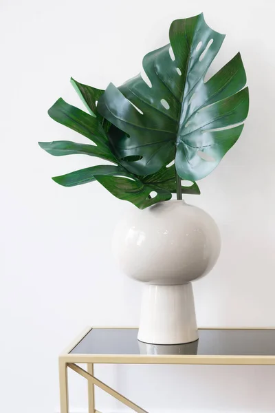 Vertical minimalistic image of a vase with monstera leaves against a white wall. Modern interior details. Stylish room decoration