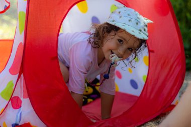 Kumaş bir evde oynayan şapkalı ve emzikli küçük kız. 