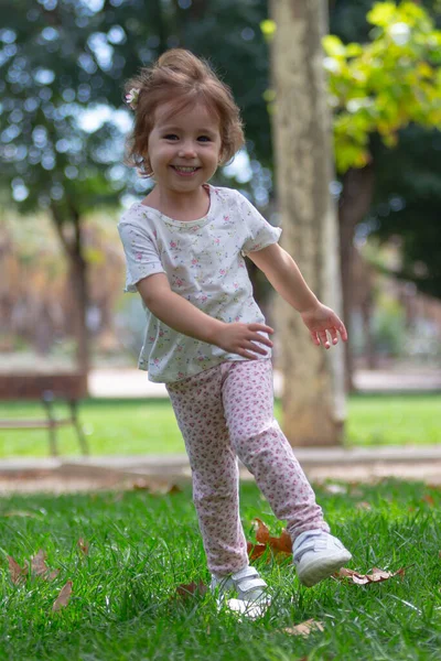 穿着裤子和T恤的金发小女孩穿过公园 — 图库照片