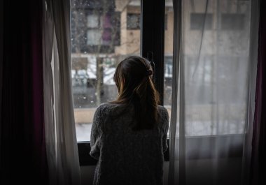 Image of a woman's back watching snowfall from a window. clipart
