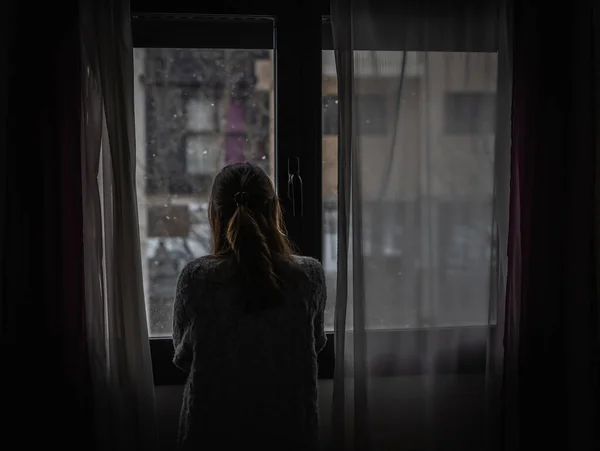 Молодая Женщина Смотрит Окно Между Занавесками Пока Идет Снег Лицензионные Стоковые Фото