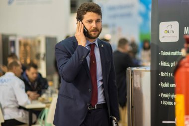Brno 'daki kongre ticaret merkezinde yürürken telefonla konuşan bir adam. BVV Brno Sergi Merkezi. Çek Cumhuriyeti
