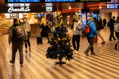 Prag, Çek Cumhuriyeti, 12-31-2020. 2020 yılının son günü COVID-19 sırasında Prag ana tren istasyonundan (Hlavni Nadrazi) ayrılmak üzere trenlerini bekleyen insanlarla çevrili Noel ağacı.