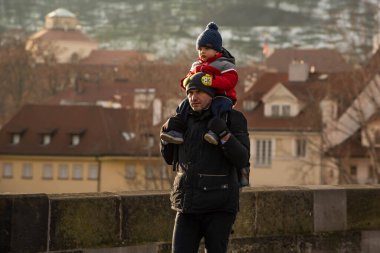 Prag, Çek Cumhuriyeti. 01-09-2021. Babası çocuğu omuzlarında tutuyor, kışın Prag 'da gün batımında Charles Köprüsü' nde yürüyor..