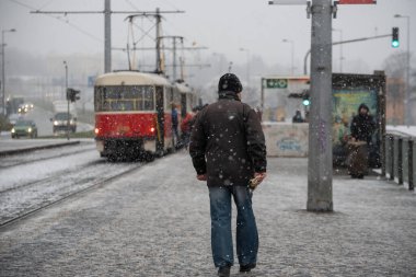 Prag, Çek Cumhuriyeti. 01-12-2021. Prag 6 'daki Hradcanska tramvay istasyonundan kalkan adam kar yağışlı bir günde maskeyle tramvaya yetişmeye çalışıyor.
