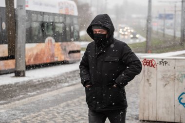 Prag, Çek Cumhuriyeti. 01-12-2021. Prag 6 'daki Hradcanska tramvay istasyonundan kalkan adam kar yağışlı bir günde maskeyle tramvaya yetişmeye çalışıyor.
