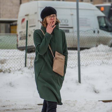 Prag, Çek Cumhuriyeti. 02-08-2021. Soğuk bir kış günü Prag 'ın merkezinde gezen şapkalı güzel, modaya uygun genç bir kadın sigara içiyor..