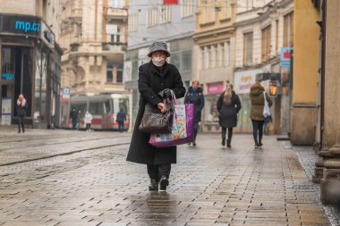Brno, Çek Cumhuriyeti. 02-17-2021. Korona virüsünden korumak için maske takan yaşlı kadın soğuk kış günü Brno şehrinde Masarykova caddesinde yürüyor..