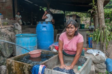 Suchitoto, El Salvador. 06-25-2016. Anne kırsal bölgedeki evde kumaş yıkıyor. Ülkenin kırsal kesimlerinde yaşayan insanlar, hayatta kalmak için sığır yetiştirmeye ve sebze yetiştirmeye bel bağlıyorlar..