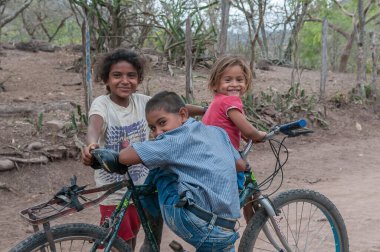 Rivas, Nicaragua. 07-15-2016. Children having fun while driving a bicycle. People living in a rural areas of the country rely on raising cattle an vegetable growth for survival. clipart