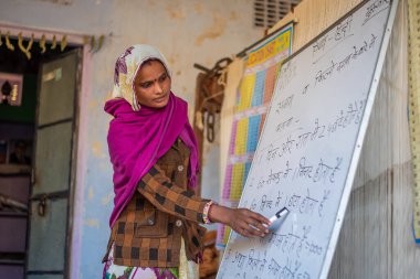 Uttar Pradesh. 05-15-2018. Kadın okulda bir kurulla ders veriyor. Tekstil endüstrisinde iplikle çalışan kadınlar. Çocuklarla ilgilenen kadınların yanı sıra, ailelerinin maddi bakımı konusunda önemli bir rolleri vardır..