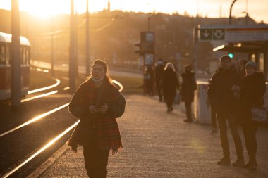 Prag, Çek Cumhuriyeti. 02-24-2021. Telefonunu kontrol eden genç bir kadın Prag şehir merkezinde yürüyor soğuk bir kış günü güzel bir gün batımıyla..