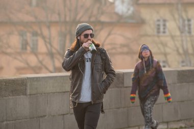 Prag, Çek Cumhuriyeti. 03-02-2021. Harika bir genç adam bira içiyor ve Prag 'ın şehir merkezindeki Charles Köprüsü' nde güzel bir günbatımıyla eğleniyor..