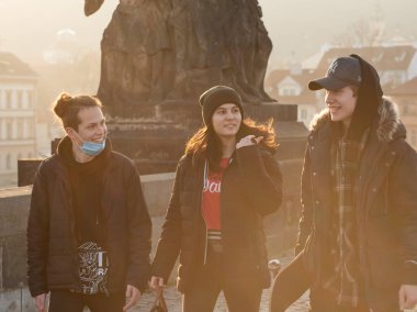 Prag, Çek Cumhuriyeti. 03-02-2021. Genç yetişkinler Prag 'ın şehir merkezindeki Charles Köprüsü' nde güzel bir gün batımıyla yürüyor, konuşuyor ve eğleniyorlar..