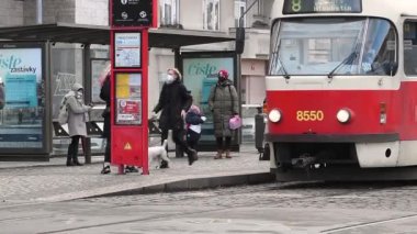 Prag, Çek Cumhuriyeti. 03-12-2021. Bir tramvay geldi ve maskeli insanlar soğuk bir kış gününde maske takarak alçalıyorlar.. 