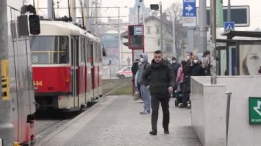 Prag, Çek Cumhuriyeti. 03-12-2021. Adam maskeyi Prag 'ın şehir merkezinde, soğuk bir kış gününde duran tramvayın yanında yürürken takıyor.. 