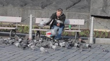 Prag, Çek Cumhuriyeti. 03-28-2021. Kulaklıklı ve bira içen bir adam Prag 'ın merkezindeki Old Town' da bir çok güvercine yemek veriyor.. 
