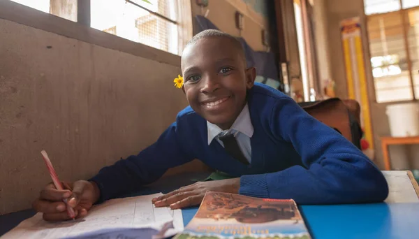 Dodoma, Tanzanya. 08-18-2019. Tanzanya 'nın kırsal kesimindeki bir okulda bankta otururken kameraya bakan, elinde çiçekle gülümseyen güzel siyahi bir kızın portresi..