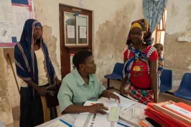 Dodoma, Tanzanya. 10-10-2018. Kırsal kesimdeki bir hastanede çalışan siyahi Müslüman personel, kliniğin girişinde tıbbi yardıma ihtiyacı olan çocuğuyla birlikte bir genci kabul ediyor..