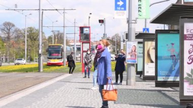 Prag, Çek Cumhuriyeti. 04-16-2021. Maskeli genç bir kadın, güneşli bir bahar gününde Prag şehrinde sarı çiçeklerle Hradcanska durağında tramvayda bekliyor..
