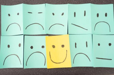 Sticky notes with unhappy smiley's and one happy smiley. On a dark grey background.
