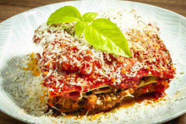 Beyaz tabakta ve ahşap arka planda çılgın lazanya bolonez. Üstünde fesleğen olan.