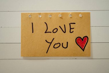 Seni seviyorum, beyaz ahşap bir arka planda bir kağıt parçasına yazılmış. Sevgililer Günü.