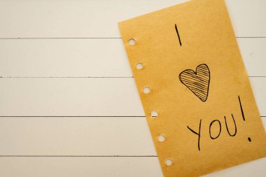 Seni seviyorum, beyaz ahşap bir arka planda bir kağıt parçasına yazılmış. Sevgililer Günü.