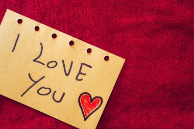 Kırmızı tekstil arka planında bir kağıt parçasına yazılmış seni seviyorum. Sevgililer Günü.