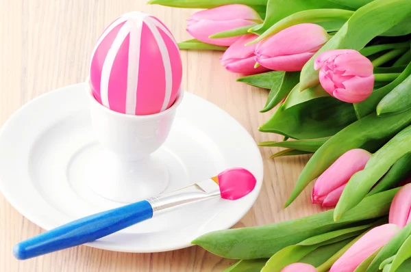 Painting pink easter egg in cup with bunch of tulips around — Stock Photo, Image