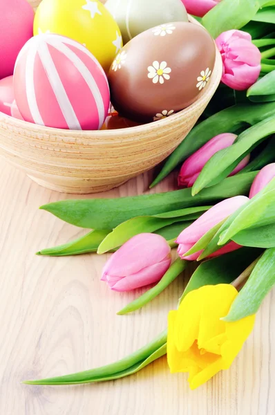 Easter eggs in a bmaboo cup with bunch of tulips around — Stock Photo, Image