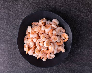 Pişmemiş portakal karidesleri siyah bir tabakta taş zemin üzerinde.