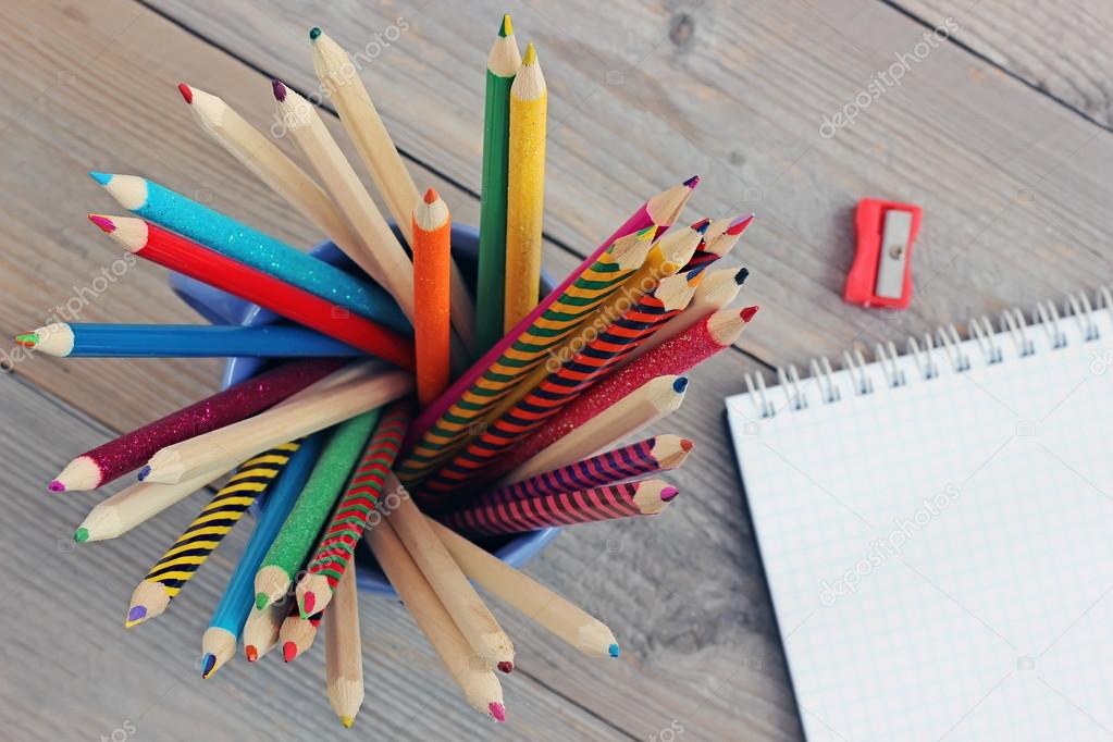 Colored pencils in a mug on wooden table, top view.