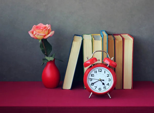 Boeken, steeg in rode vaas en rode retro wekker op tafel met — Stockfoto