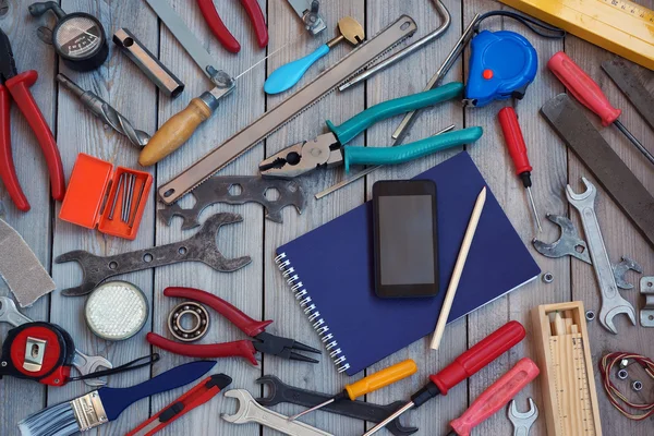 Notepad, mobile phone and tools on a wooden floor, top view.