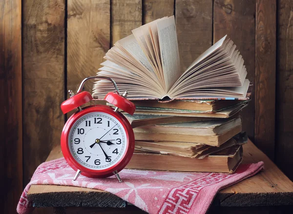 Reloj despertador rojo retro y una pila de libros sobre la mesa . — Foto de Stock