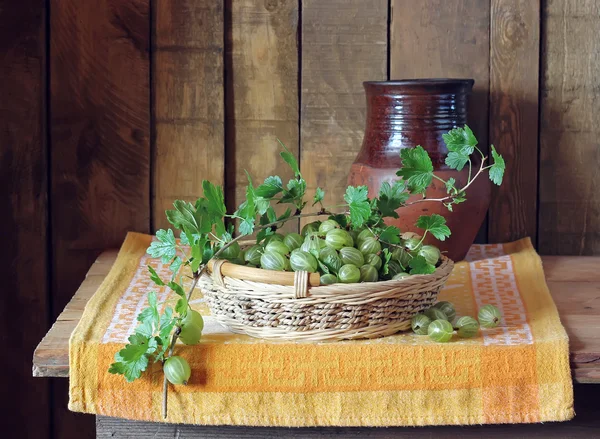 Still life with a basket of gooseberries and a jug. — Stock Photo, Image