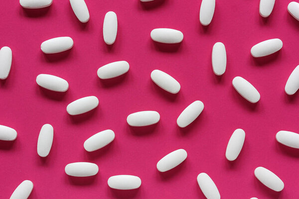white tablets on a pink background, top view. medical background, flat lay. 