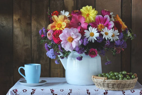 ティーポットの花の花束とバスケットの緑のグーズベリーと暗い背景のテーブルの上のマグカップでまだ生活 — ストック写真