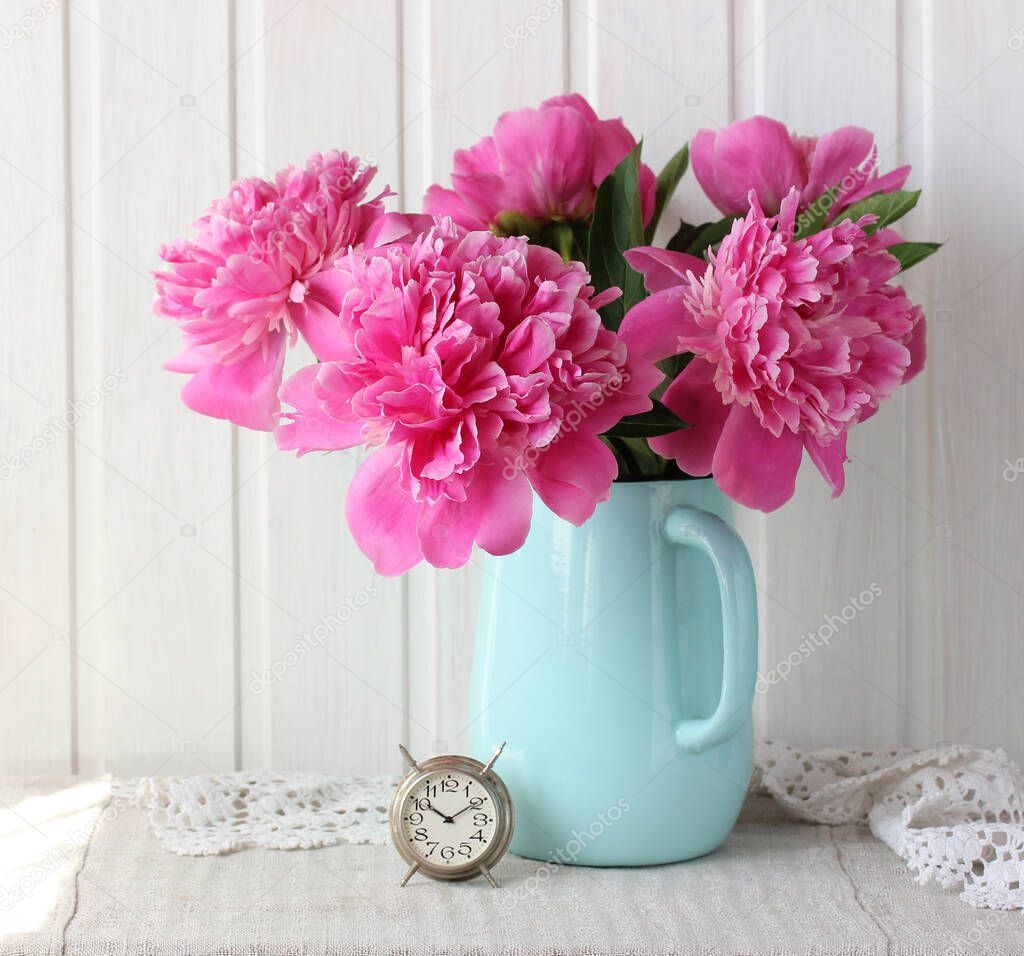 bouquet of pink peonies in a jug and an alarm clock. garden flowers.