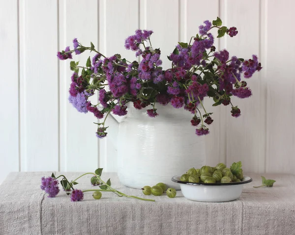 紫のアゲラテムと緑のグーズベリー まだ花や果実と共に生きています 素朴なスタイルで構成され — ストック写真
