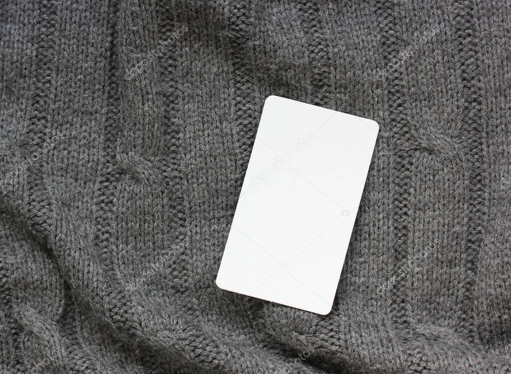 one empty white card on a knitted gray background, top view. mockup, scene creator.