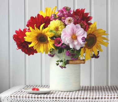 Bir buket ayçiçeği ve yıldız çiçeği. Masada çiçekler ve ahududular var. Kırsal bir iç mekanda ışık bileşimi.