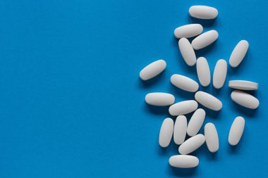 Mavi arka planda beyaz tabletler, üst manzara. Tıbbi zemin, düz yatış. Boşluğu kopyala. 