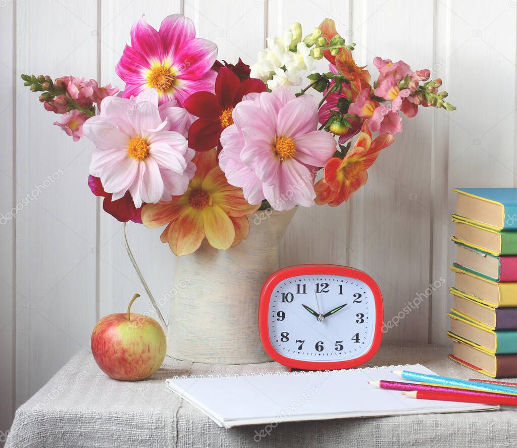 back to school. autumn composition with a bouquet of dahlias, textbooks and an alarm clock on the table.