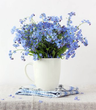 Masanın üzerinde beyaz bir kupada mavi beni unutma. Yaz bahçesi buketi.