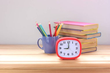 kırmızı alarmlı saat, bir yığın ders kitabı ve renkli kalemler masanın üzerinde..