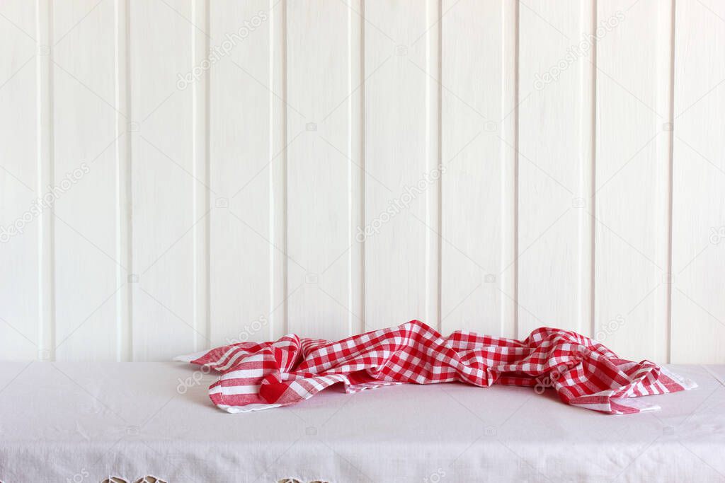 an empty table with a tablecloth and a red towel against a white wall. kitchen background, copy space.